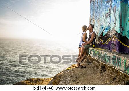 Stock Photograph - Caucasian couple kissing at mural on cliff. Fotosearch