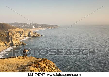 Stock Photo - Caucasian couple on cliff admiring seascape . Fotosearch