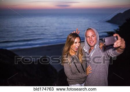 Stock Image - Caucasian couple taking selfie at beach. Fotosearch