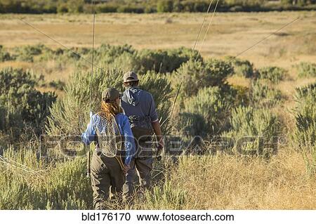 Stock Image - Caucasian couple with fishing gear in field. Fotosearch