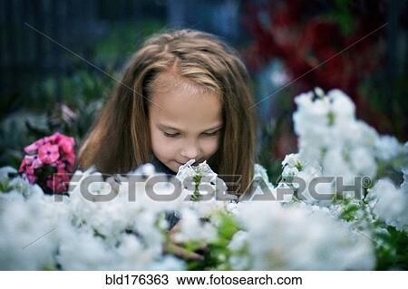 Stock Image - Caucasian girl smelling flowers in garden. Fotosearch