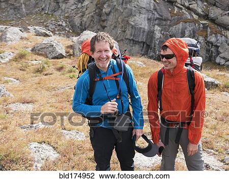 Stock Image - Caucasian hikers smiling on hillside. Fotosearch
