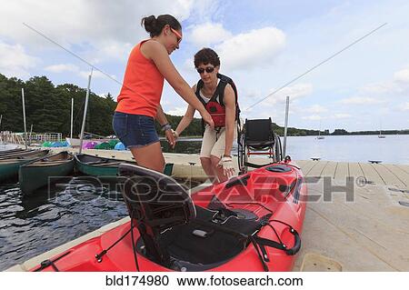 Stock Image - Caucasian instructor helping paraplegic woman with kayak. Fotosearch