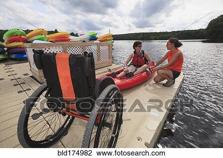 Stock Image - Caucasian instructor helping paraplegic woman with kayak. Fotosearch
