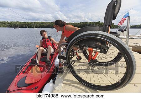 Stock Photo - Caucasian instructor helping paraplegic woman with kayak. Fotosearch