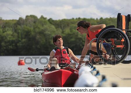 Stock Photograph - Caucasian instructor helping paraplegic woman with kayak. Fotosearch
