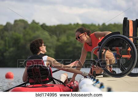 Stock Photography - Caucasian instructor helping paraplegic woman with kayak. Fotosearch
