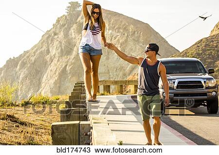 Stock Image - Caucasian man assisting woman walking on railing. Fotosearch