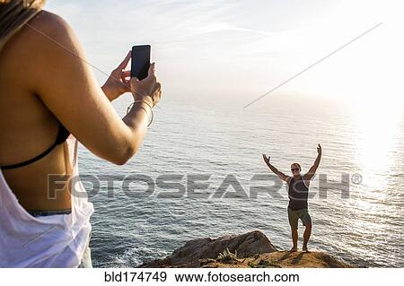 Stock Photo - Caucasian man photographing girlfriend on cliff. Fotosearch