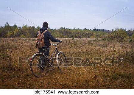 Stock Image - Caucasian man pushing bicycle in field. Fotosearch