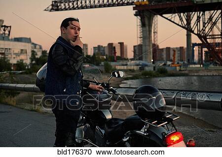 Stock Image - Caucasian man smoking near motorcycle. Fotosearch