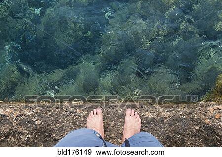 Stock Photo - Caucasian man standing on rock wall over water. Fotosearch
