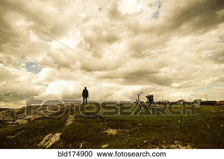 Stock Image - Caucasian man with bicycle in field. Fotosearch