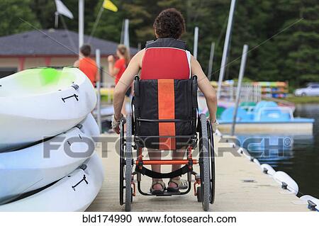 Stock Image - Caucasian paraplegic woman sitting on dock. Fotosearch