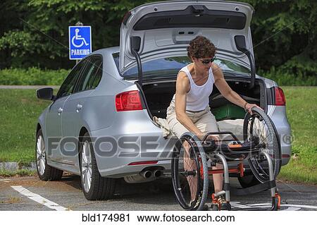 Stock Image - Caucasian paraplegic woman unloading wheelchair from car. Fotosearch