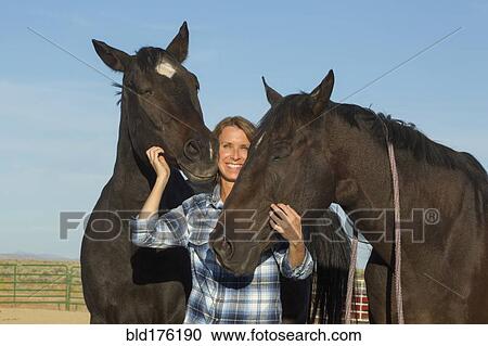 Stock Image - Caucasian rancher smiling with horses. Fotosearch