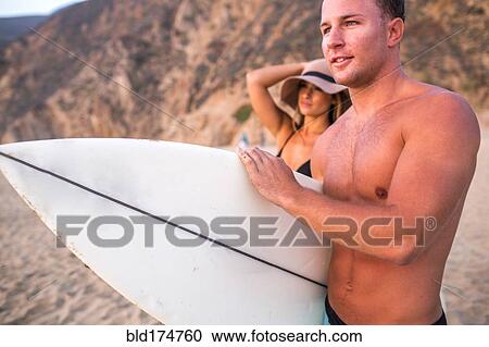 Stock Image - Caucasian surfer carrying surfboard on beach. Fotosearch