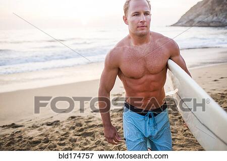 Stock Photo - Caucasian surfer carrying surfboard on beach. Fotosearch