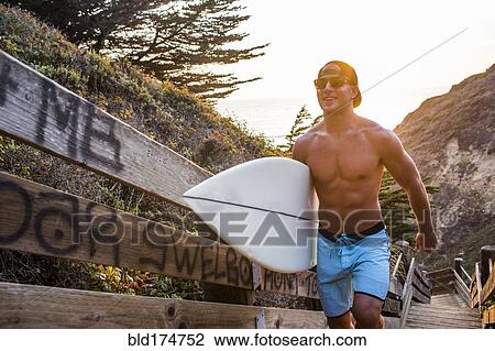 Stock Image - Caucasian surfer carrying surfboard. Fotosearch
