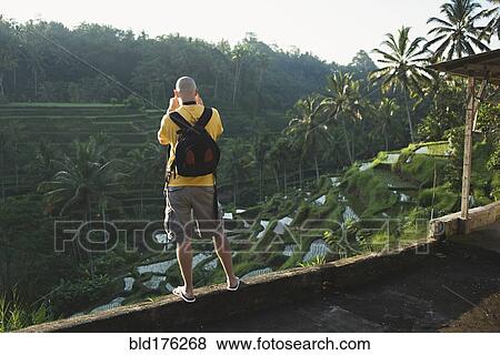 Stock Photo - Caucasian tourist photographing rural rice terrace, Ubud, Bali, Indonesia. Fotosearch