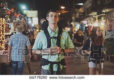 Stock Image - Caucasian tourist standing in market at night. Fotosearch