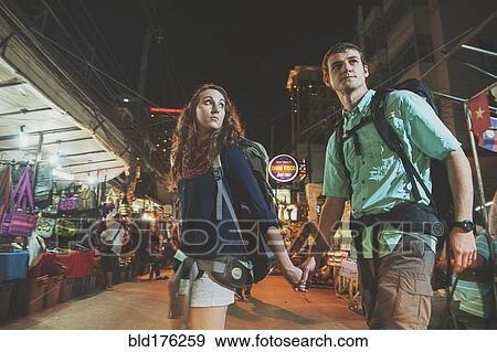 Stock Photo - Caucasian tourists holding hands in market at night. Fotosearch