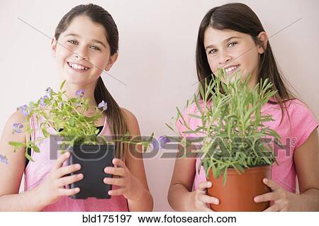 Stock Photo - Caucasian twin sisters holding potted plants. Fotosearch