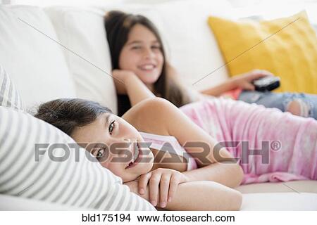 Picture - Caucasian twin sisters laying on sofa. Fotosearch