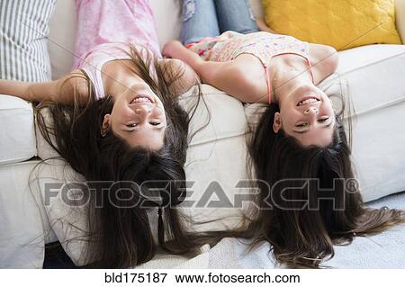 Stock Photo - Caucasian twin sisters laying on sofa. Fotosearch