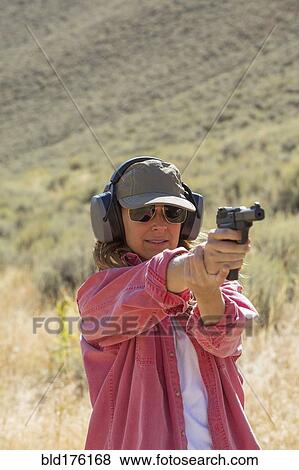 Stock Photo - Caucasian woman aiming gun outdoors. Fotosearch