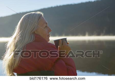Stock Photograph - Caucasian woman drinking coffee at lake. Fotosearch