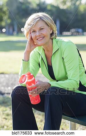 Stock Image - Caucasian woman drinking water bottle in park. Fotosearch