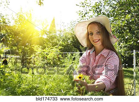 Stock Image - Caucasian woman examining plants in garden. Fotosearch