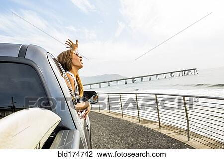 Stock Image - Caucasian woman leaning out car window at beach. Fotosearch