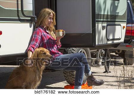 Stock Image - Caucasian woman petting dog at trailer. Fotosearch