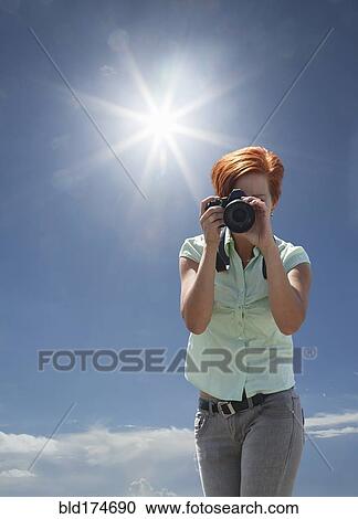 Stock Image - Caucasian woman photographing under blue sky. Fotosearch