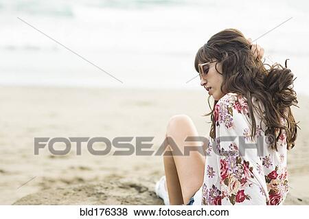 Stock Photo - Caucasian woman sitting in sand on beach. Fotosearch