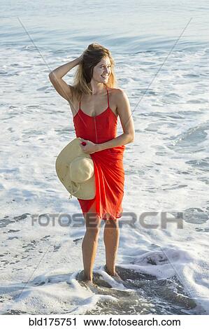 Stock Image - Caucasian woman standing in waves on beach. Fotosearch