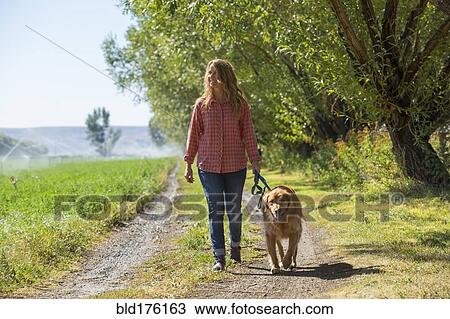 Stock Image - Caucasian woman walking dog on dirt path. Fotosearch