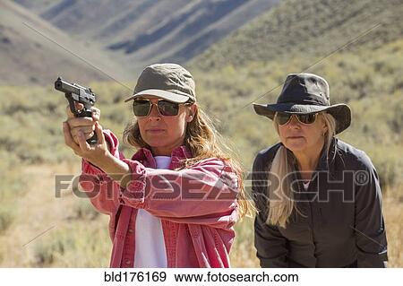 Stock Photo - Caucasian women aiming gun outdoors. Fotosearch