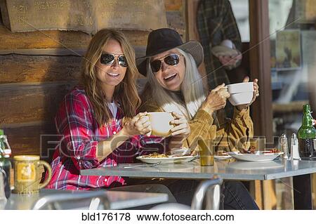 Stock Photo - Caucasian women drinking coffee at cafe. Fotosearch