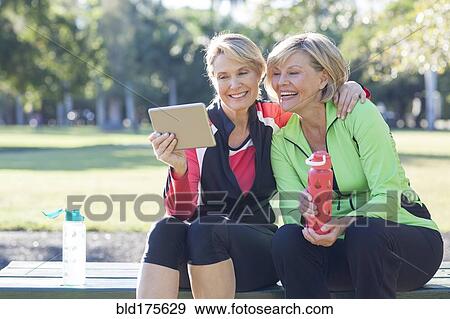 Caucasian women using digital tablet in park View Large Photo Image Stock Photo - Caucasian women using digital tablet in park. Fotosearch