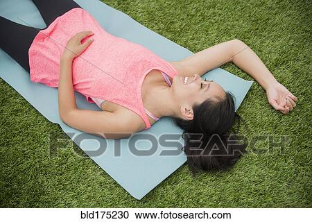 Stock Image - Chinese woman laying on yoga mat in grass. Fotosearch