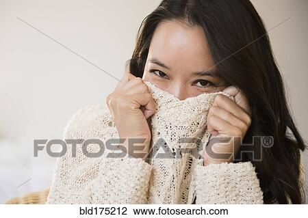 Stock Image - Chinese woman peeking over collar of sweater. Fotosearch