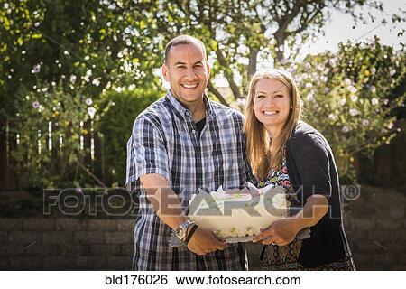 Stock Photograph - Couple holding cake at engagement party. Fotosearch