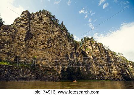 Stock Image - Distant boat on river near cliff. Fotosearch