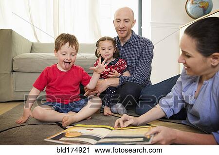 Stock Image - Family reading book on floor in living room. Fotosearch