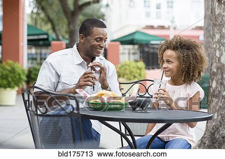 Stock Image - Father and daughter eating at outdoor restaurant table. Fotosearch