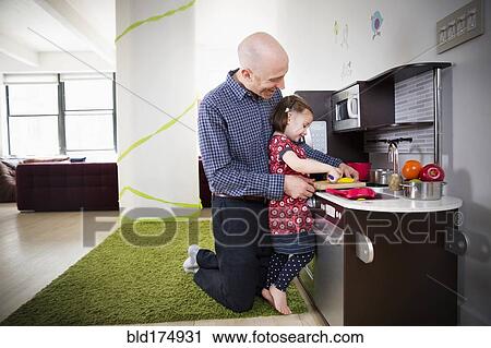 Stock Image - Father and daughter playing in toy kitchen. Fotosearch