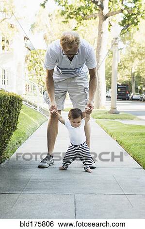 Father helping baby son walk on sidewalk View Large Photo Image Stock Photograph - Father helping baby son walk on sidewalk. Fotosearch